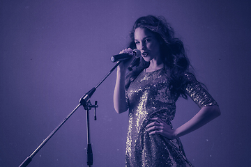 Image showing Caucasian female singer portrait isolated on purple studio background in neon light