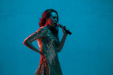 Image showing Caucasian female singer portrait isolated on blue studio background in neon light