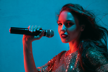 Image showing Caucasian female singer portrait isolated on blue studio background in neon light