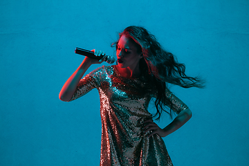 Image showing Caucasian female singer portrait isolated on blue studio background in neon light