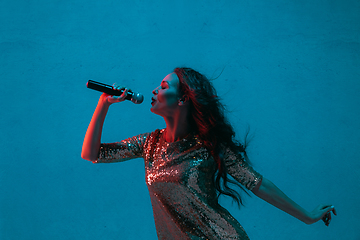 Image showing Caucasian female singer portrait isolated on blue studio background in neon light