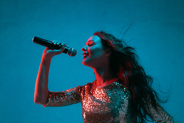 Image showing Caucasian female singer portrait isolated on blue studio background in neon light