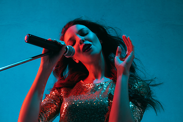 Image showing Caucasian female singer portrait isolated on blue studio background in neon light