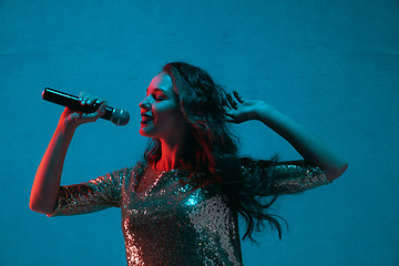 Image showing Caucasian female singer portrait isolated on blue studio background in neon light