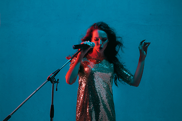 Image showing Caucasian female singer portrait isolated on blue studio background in neon light