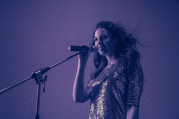 Image showing Caucasian female singer portrait isolated on purple studio background in neon light