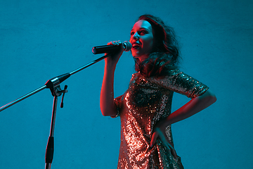 Image showing Caucasian female singer portrait isolated on blue studio background in neon light