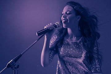 Image showing Caucasian female singer portrait isolated on purple studio background in neon light