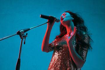 Image showing Caucasian female singer portrait isolated on blue studio background in neon light