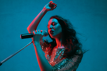 Image showing Caucasian female singer portrait isolated on blue studio background in neon light