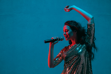 Image showing Caucasian female singer portrait isolated on blue studio background in neon light