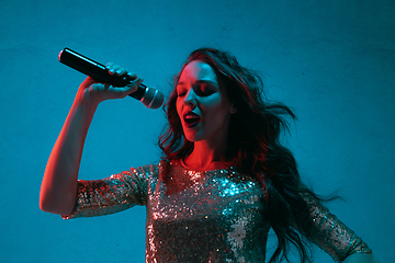 Image showing Caucasian female singer portrait isolated on blue studio background in neon light