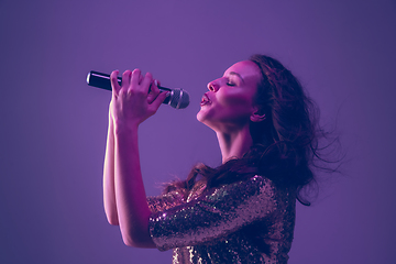 Image showing Caucasian female singer portrait isolated on purple studio background in neon light