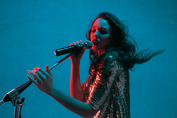 Image showing Caucasian female singer portrait isolated on blue studio background in neon light