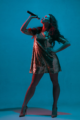 Image showing Caucasian female singer portrait isolated on blue studio background in neon light