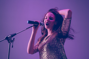 Image showing Caucasian female singer portrait isolated on purple studio background in neon light