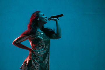 Image showing Caucasian female singer portrait isolated on blue studio background in neon light