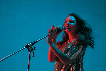 Image showing Caucasian female singer portrait isolated on blue studio background in neon light