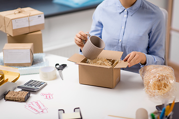 Image showing woman packing mug to parcel box at post office