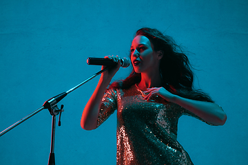 Image showing Caucasian female singer portrait isolated on blue studio background in neon light