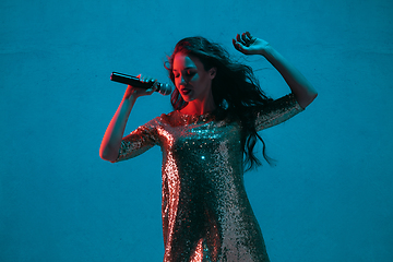 Image showing Caucasian female singer portrait isolated on blue studio background in neon light
