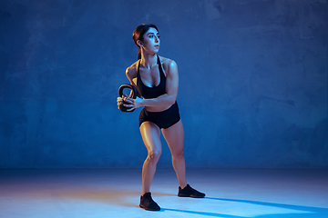 Image showing Caucasian young female athlete practicing on blue studio background in neon light