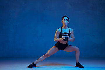 Image showing Caucasian young female athlete practicing on blue studio background in neon light