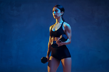 Image showing Caucasian young female athlete practicing on blue studio background in neon light
