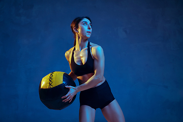 Image showing Caucasian young female athlete practicing on blue studio background in neon light