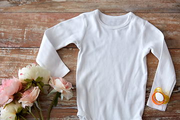 Image showing baby bodysuit with soother and flowers on wood