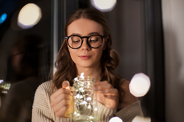 Image showing woman with garland lights in glass mug at home