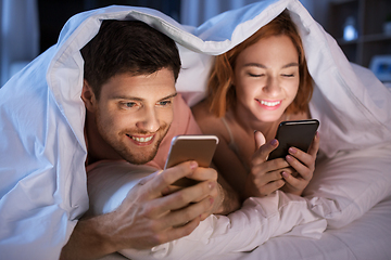 Image showing happy couple using smartphones in bed at night