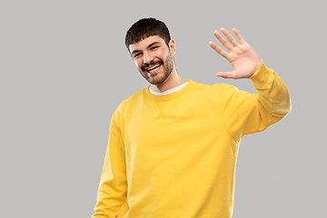 Image showing smiling young man in yellow sweatshirt waving hand