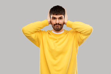 Image showing man in yellow sweatshirt closing ears by hands