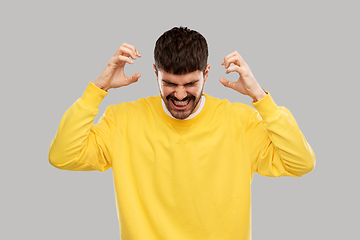 Image showing angry young man in yellow sweatshirt over grey