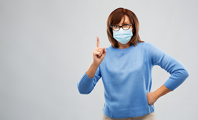 Image showing senior woman in medical mask pointing finger up