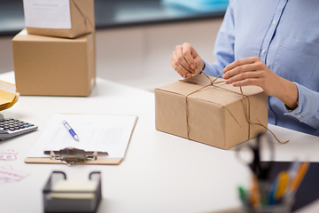 Image showing woman packing parcel and tying rope at post office