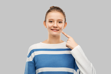 Image showing smiling teenage girl pointing finger to her face