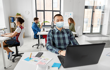 Image showing man in medical mask with laptop working at office