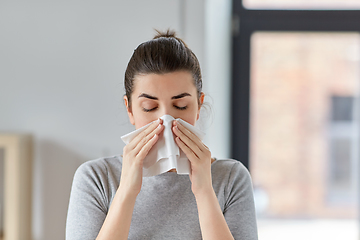 Image showing sick woman blowing nose in paper tissue at home