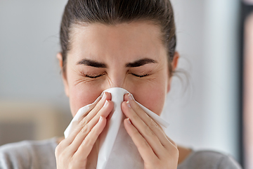 Image showing sick woman blowing nose in paper tissue at home