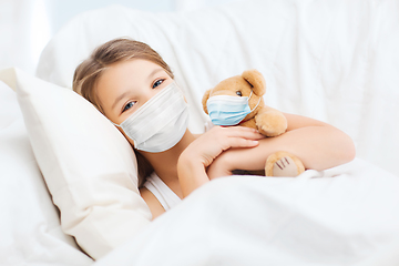 Image showing girl wearing medical mask with teddy bear in bed