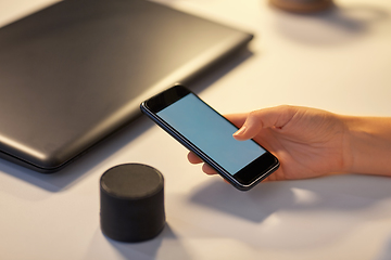 Image showing hand with smartphone and smart speaker at office