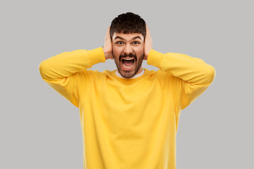 Image showing man in yellow sweatshirt closing ears by hands