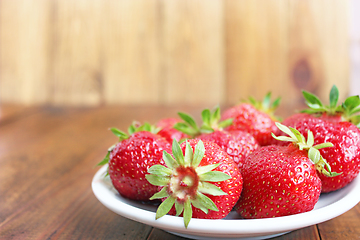 Image showing ripe red strawberries on the white plate on the brown