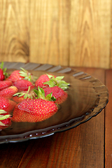 Image showing ripe red strawberries in the water on the plate on the brown