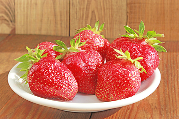 Image showing ripe red strawberries on the white plate on the brown