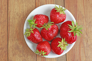 Image showing ripe red strawberries on the white plate on the brown