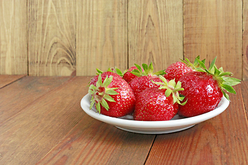 Image showing ripe red strawberries on the white plate on the brown