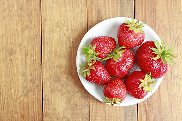 Image showing ripe red strawberries on the white plate on the brown